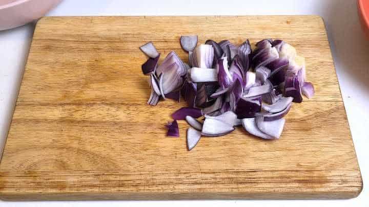 Diced red onion on a wooden chopping board for hoisin chicken noodles.