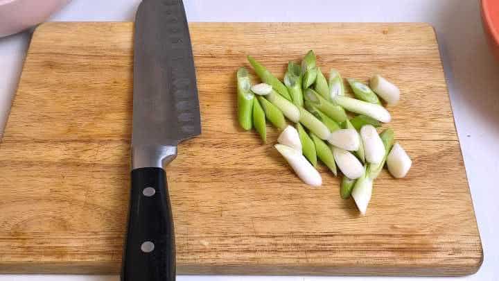 Spring onions cut into 1-inch pieces on a wooden chopping board.