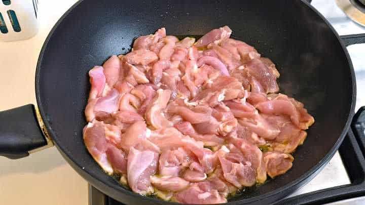 Stir-frying chicken thigh strips with high-heat cooking oil in a wok.