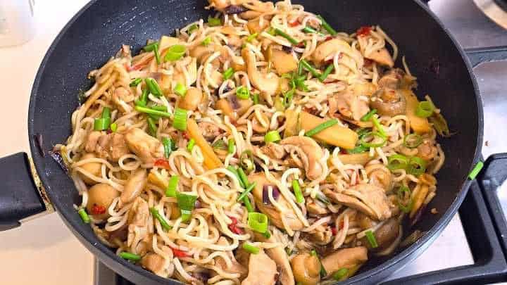 Fresh egg noodles tossed with hoisin chicken and stir-fried vegetables in a wok ready to serve.