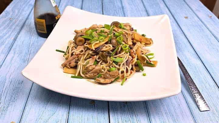 A bowl of takeout-style hoisin chicken noodles garnished with fresh chives.