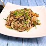 Freshly made easy hoisin chicken noodles garnished with chopped chives and spring onions served on a deep white plate.