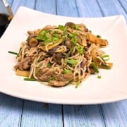 Freshly made easy hoisin chicken noodles garnished with chopped chives and spring onions served on a deep white plate.