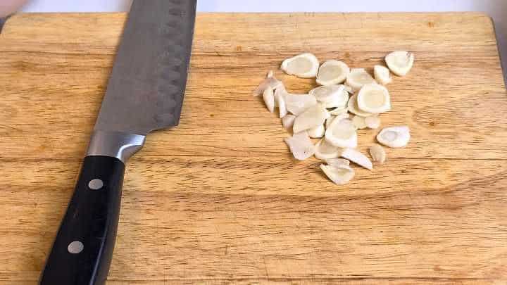 Thinly sliced garlic cloves on a chopping board for wok stir-frying.