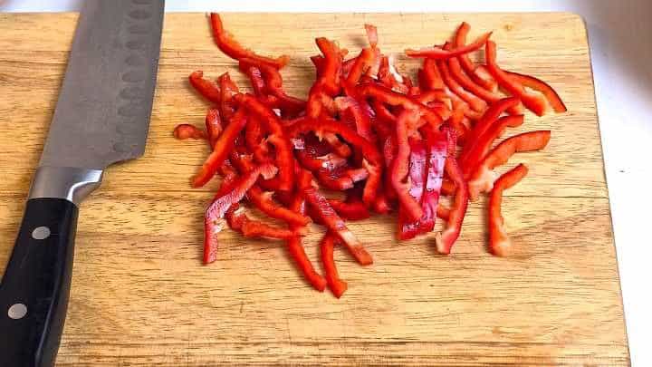 Thinly sliced red kapia pepper on a chopping board prepped for stir fry.