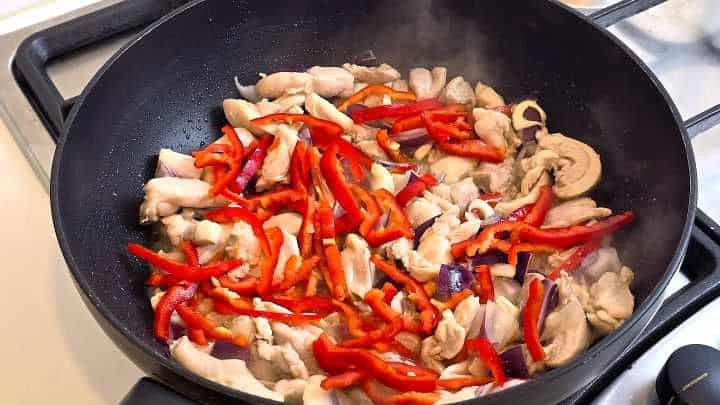 Stir-frying chicken, garlic, and red pepper strips in a wok with seasonings.