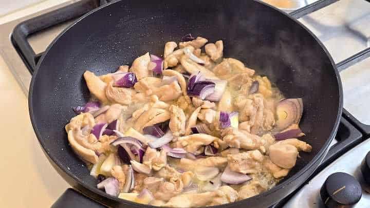 Adding diced red onion to chicken thigh strips in a wok.