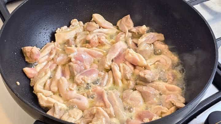 Searing chicken thigh strips in a hot wok until no longer pink.