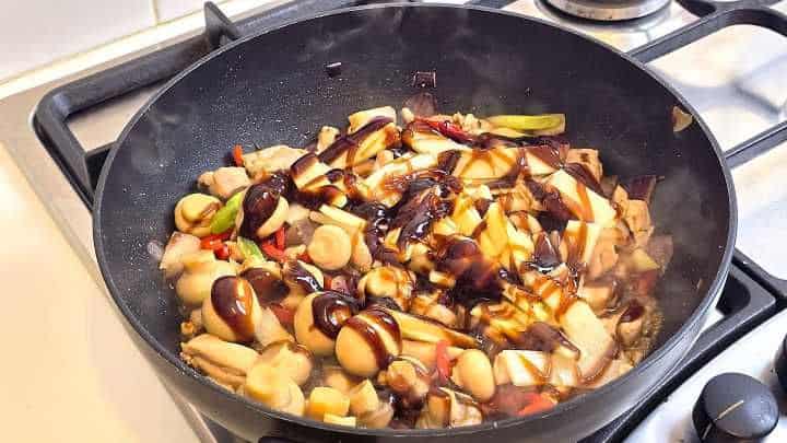 Tossing chicken and vegetables in rich hoisin sauce and dark soy sauce in a wok.