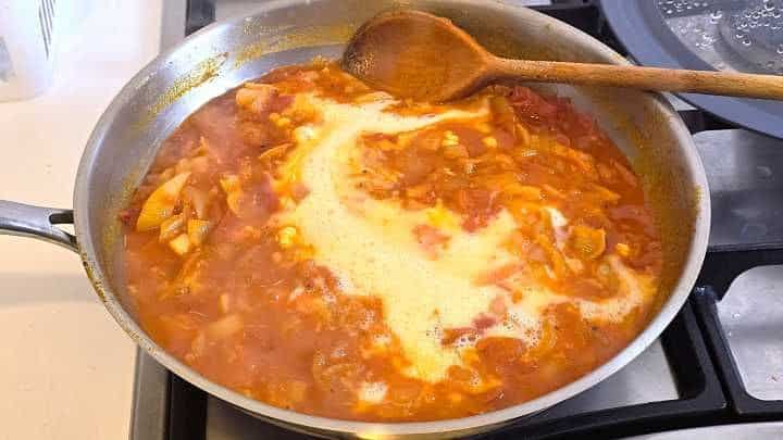 Pouring lightly beaten eggs over simmering Hungarian pepper and tomato stew.