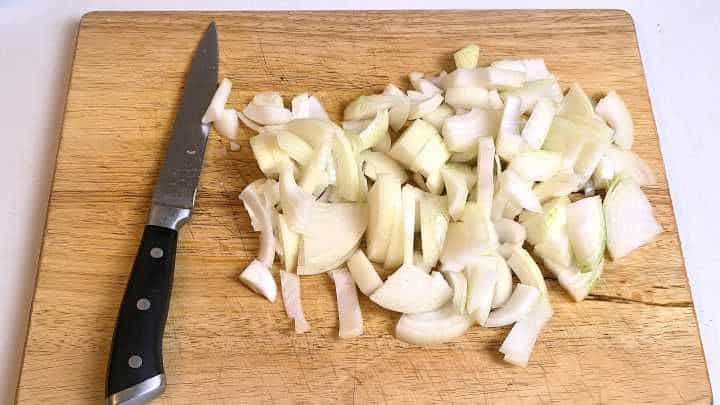 Thinly sliced onions on a wooden chopping board prepared for Hungarian vegetable stew.