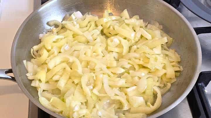 Sautéing sliced wax peppers alongside translucent onions and fresh garlic in a pan.