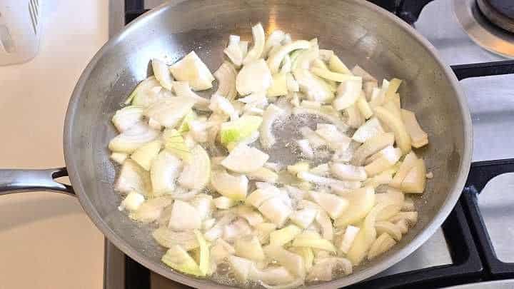 Sautéing sliced onions in melted pork lard in a skillet over medium heat.