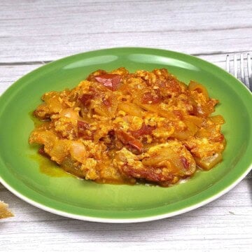 Authentic Hungarian vegetable stew with eggs (Tojásos Lecsó) served on a green plate with crusty bread slices.
