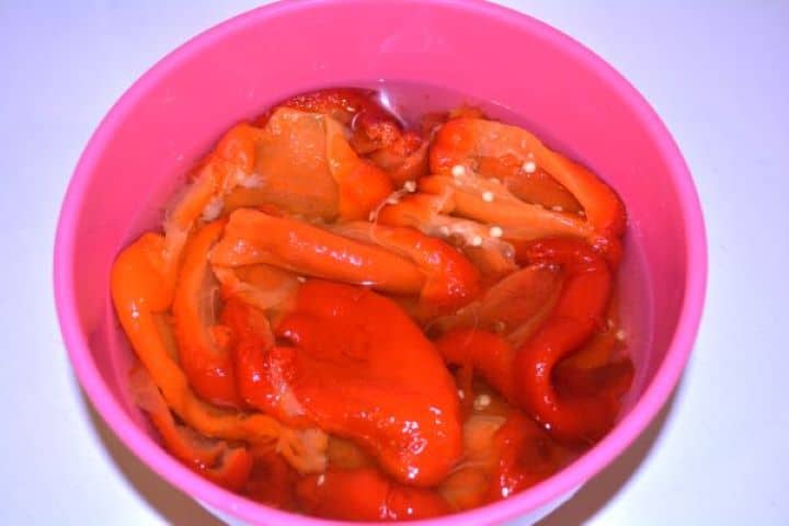 Marinated Roasted Red Peppers-Roasted Red Bell Peppers Marinating in the Bowl Peeled roasted red peppers submerged in tangy vinegar marinade in a bowl.