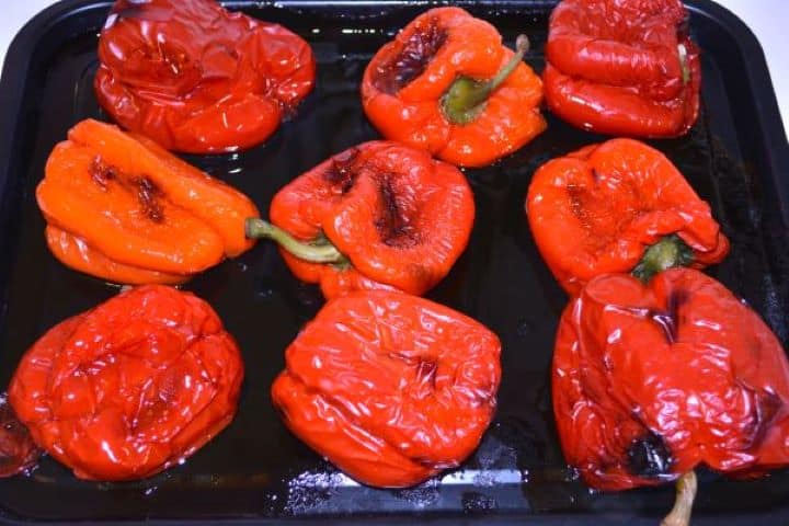 Marinated Roasted Red Peppers-Roasted Red Bell Peppers in the Baking Sheet Oven roasted red bell peppers with wrinkled blistered skins on a baking sheet.
