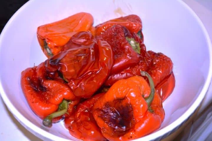Hot roasted red bell peppers steaming in a bowl covered with aluminum foil.