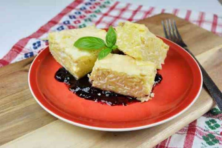 Sweet Noodle Kugel With Raisins Served on Red Plate With Blueberry Jam on Bottom