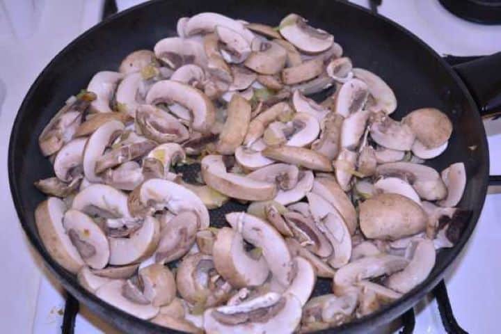 Mushrooms Adding sliced white button mushrooms to softened onions in a skillet.