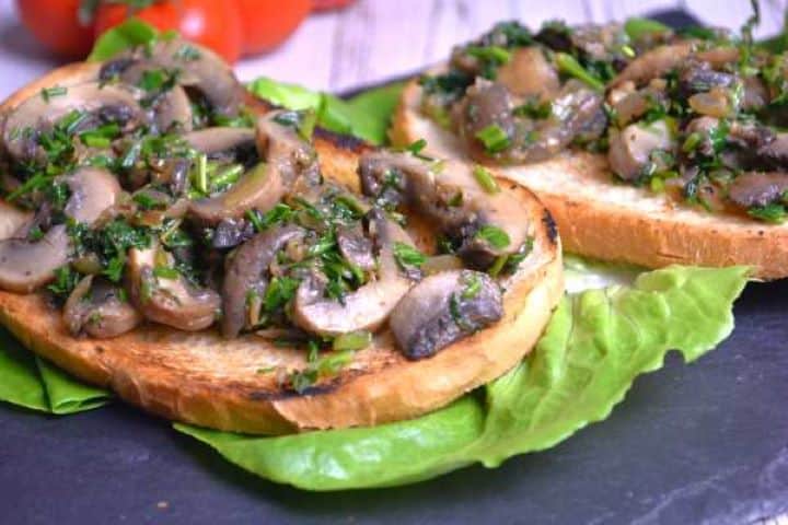 Serve Close-up view of golden sautéed garlic mushrooms garnished with fresh green herbs.