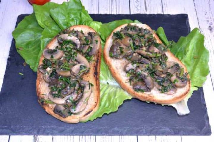 Served Warm vegan garlic mushrooms served on a white plate as a tapas appetizer with sliced toasted bread.