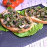 Sautéed vegan garlic mushrooms served on a plate with toasted crusty bread, crisp lettuce, and cherry tomatoes.