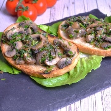 Sautéed vegan garlic mushrooms served on a plate with toasted crusty bread, crisp lettuce, and cherry tomatoes.
