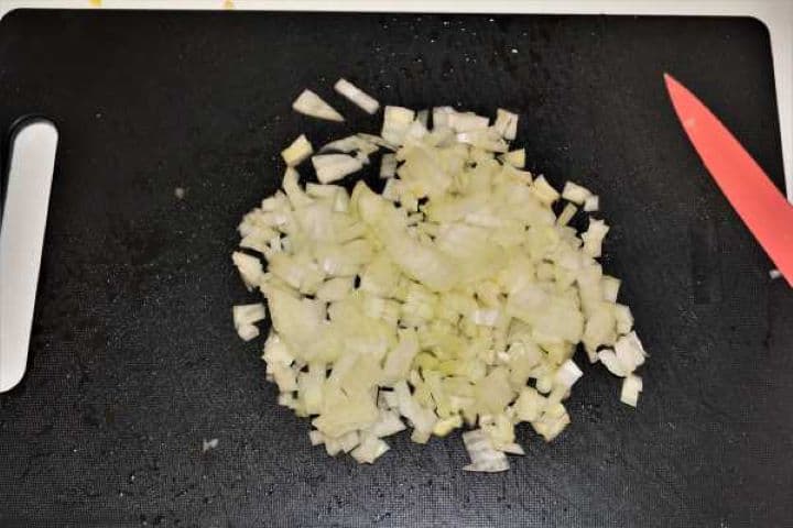 Finely diced yellow onion on a black cutting board for pork pasta sauce prep