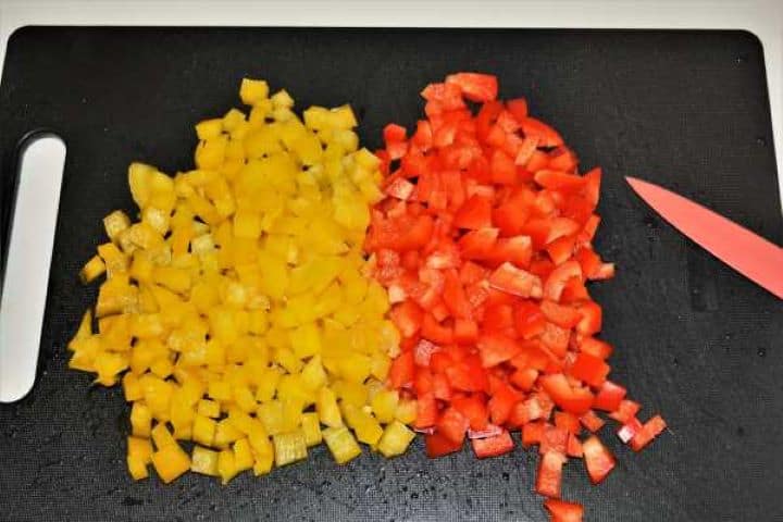 Diced red and yellow bell peppers ready for sautéing on a black cutting board.