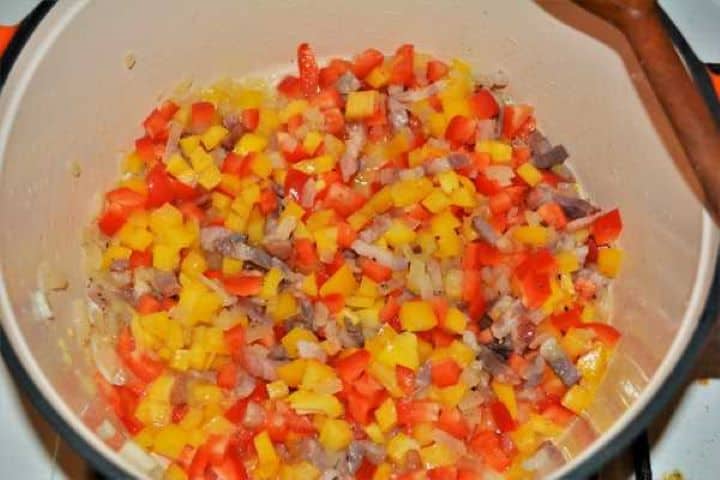 Red and yellow bell peppers cooking with onions and bacon for pork ragù.