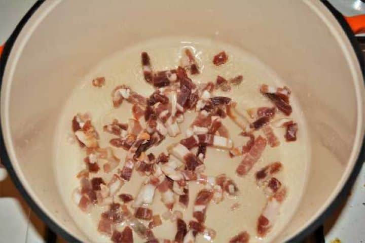 Crispy smoked bacon pieces sizzling in oil in a cast iron pot.