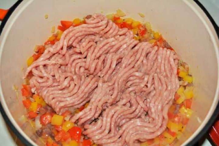Pork mince added to sautéed bacon, onions, and bell peppers in a skillet.