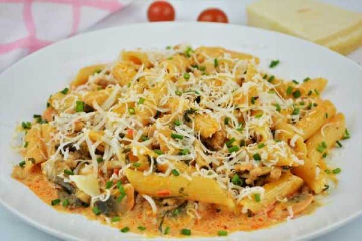 Bowl of creamy Hungarian-inspired ground pork pasta with mushrooms garnished with grated Parmesan and fresh chives.