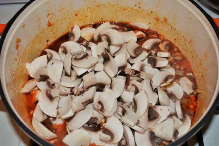 Sliced mushrooms added to browned pork mince in a skillet.
