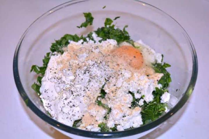 Adding crumbled Greek feta, softened cream cheese, and a raw egg to chopped spinach and leeks.