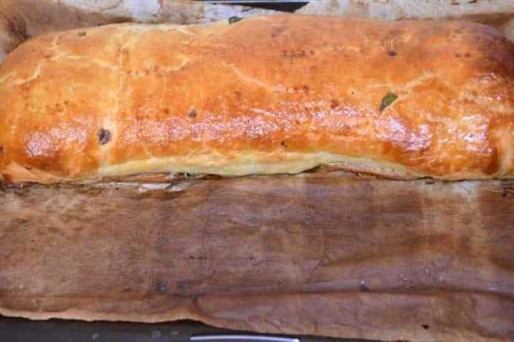 Freshly baked golden brown puff pastry spinach roll resting on parchment paper.