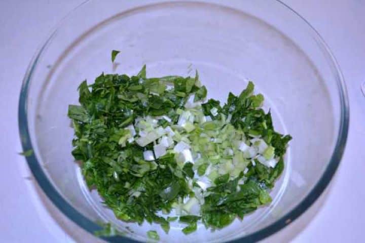 Finely chopped raw spinach and quartered leeks combined in a glass mixing bowl.