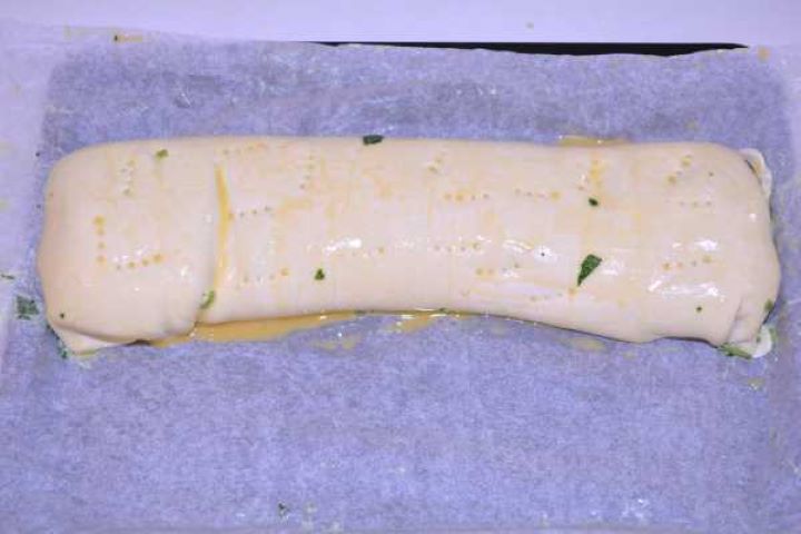 Sheet of puff pastry spread with spinach feta filling and tightly rolled into a log.