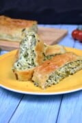 Slices of warm puff pastry spinach and feta rolls showing the creamy center on a yellow plate.