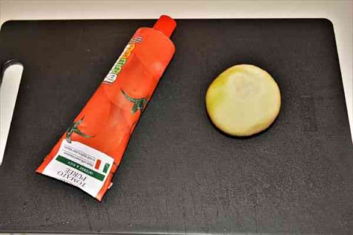Onion and Tomato Puree Whole yellow onion and concentrated tomato paste on a wooden chopping board