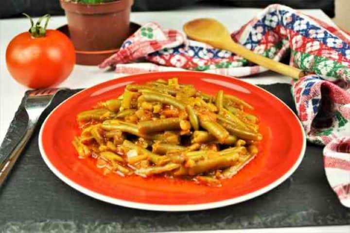 Serve Green beans in rich tomato sauce on a red plate with a wooden spoon.