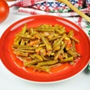 Greek green beans in tomato sauce served on a red plate with fresh bread.