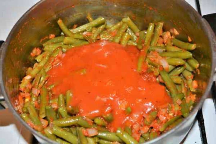 Tomato Sauce Pouring seasoned tomato sauce over green beans in a saucepan.