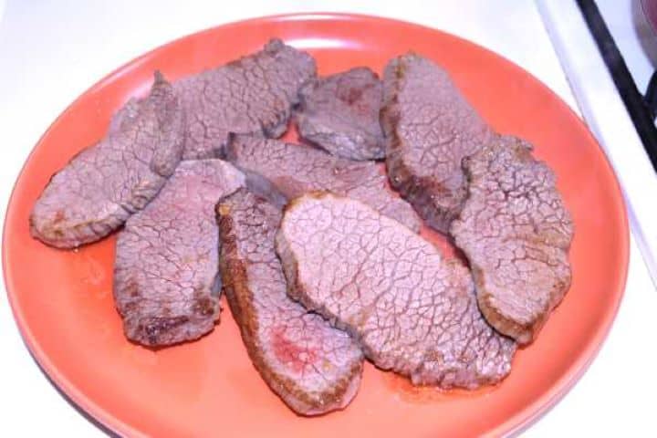 Remove Browned seared beef slices resting on a plate before simmering.