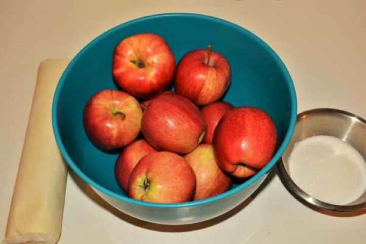 Apple Shortcrust Pastry Recipe-Apples, Shortcrust Pastry and Sugar Ingredients laid out on a kitchen counter for an apple shortcrust pastry recipe, including whole red apples, a sheet of ready-rolled shortcrust pastry, and sugar.