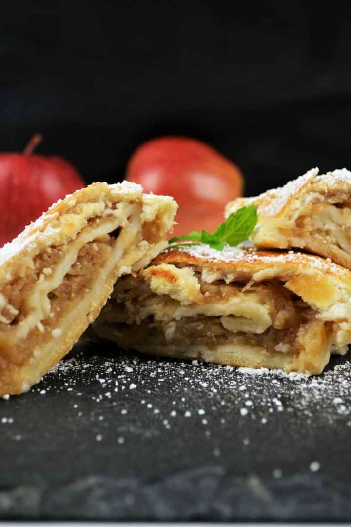 Golden baked apple shortcrust pastry roll sliced on a platter dusted with icing sugar