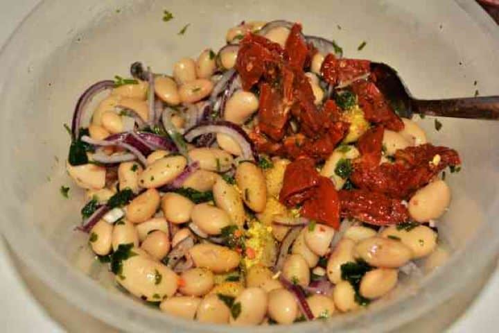 Butter Beans Salad Recipe-Chopped Sundried Tomatoes Over Ingredients in the Bowl Adding chopped sun-dried tomatoes into the butter bean salad mixture.
