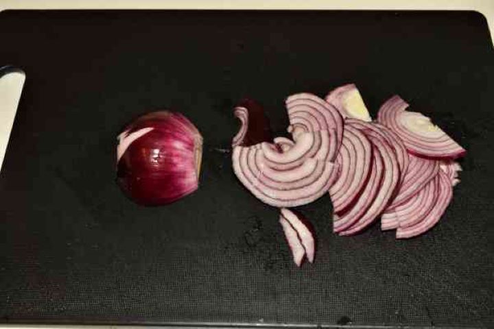 Butter Beans Salad Recipe-Sliced Red Onion Thinly sliced red onion on a black cutting board for bean salad prep.