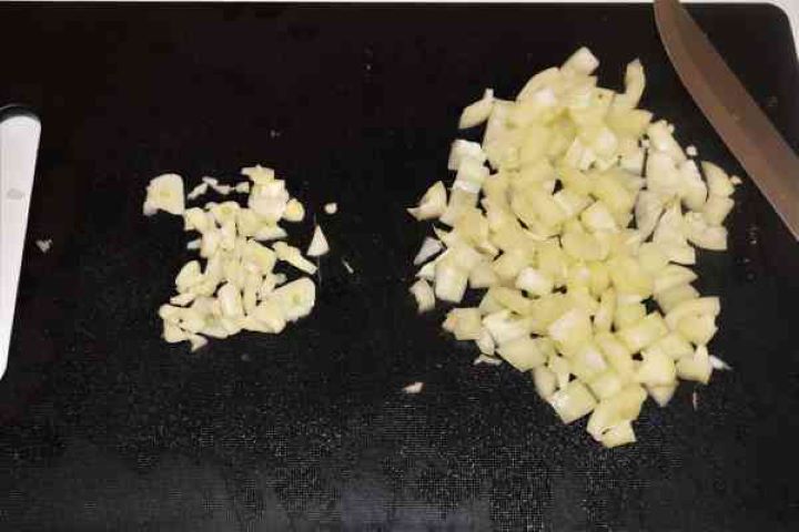 Dutch Oven Beef Stew-Chopped Yellow Pepper and Chopped Garlic Cloves Finely diced yellow bell pepper and minced fresh garlic cloves on a black chopping board for a stew base.