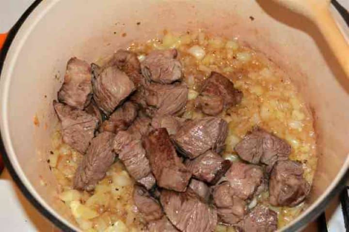 Dutch Oven Beef Stew-Fried Beef Cubes Over Frying Vegetables in the Dutch Oven Adding seared beef braising steak back into a Dutch oven pot with translucent sautéed onions and yellow peppers.